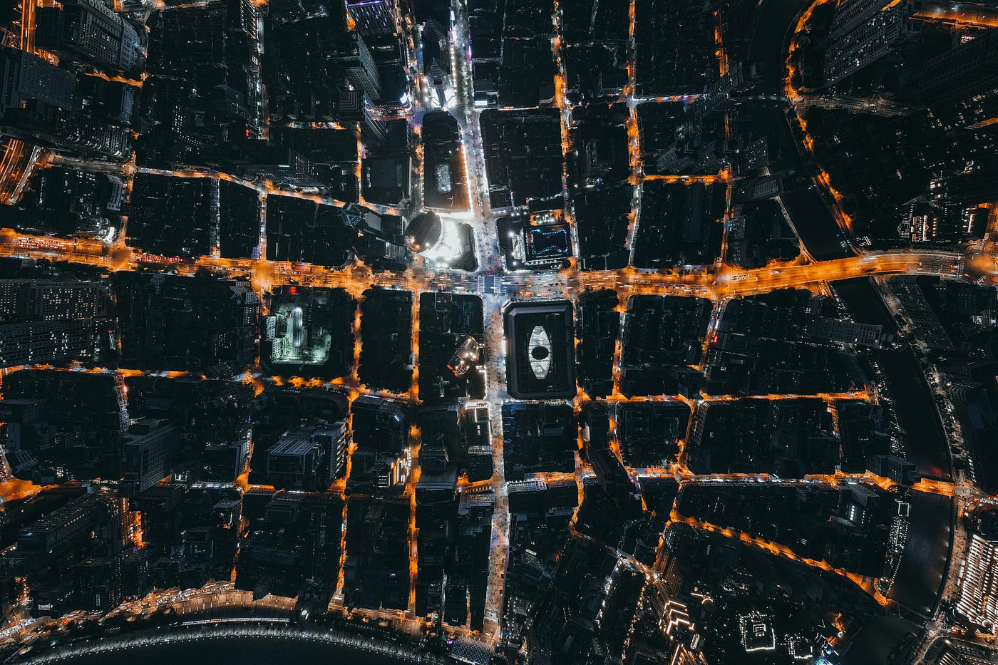 Aerial photograph of a city at night, with illuminated streets forming a grid around dark city blocks.